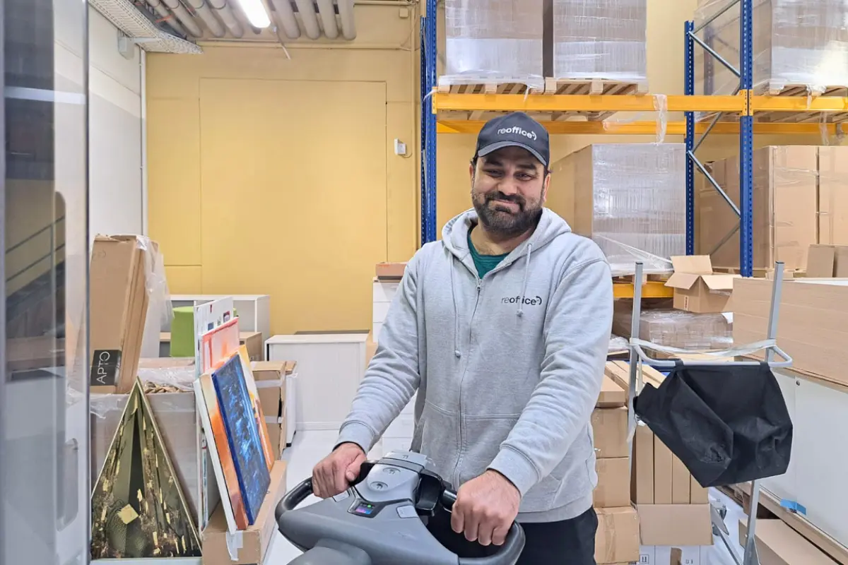 Ein lächelnder Reoffice-Mitarbeiter bedient einen Hubwagen im Lager.