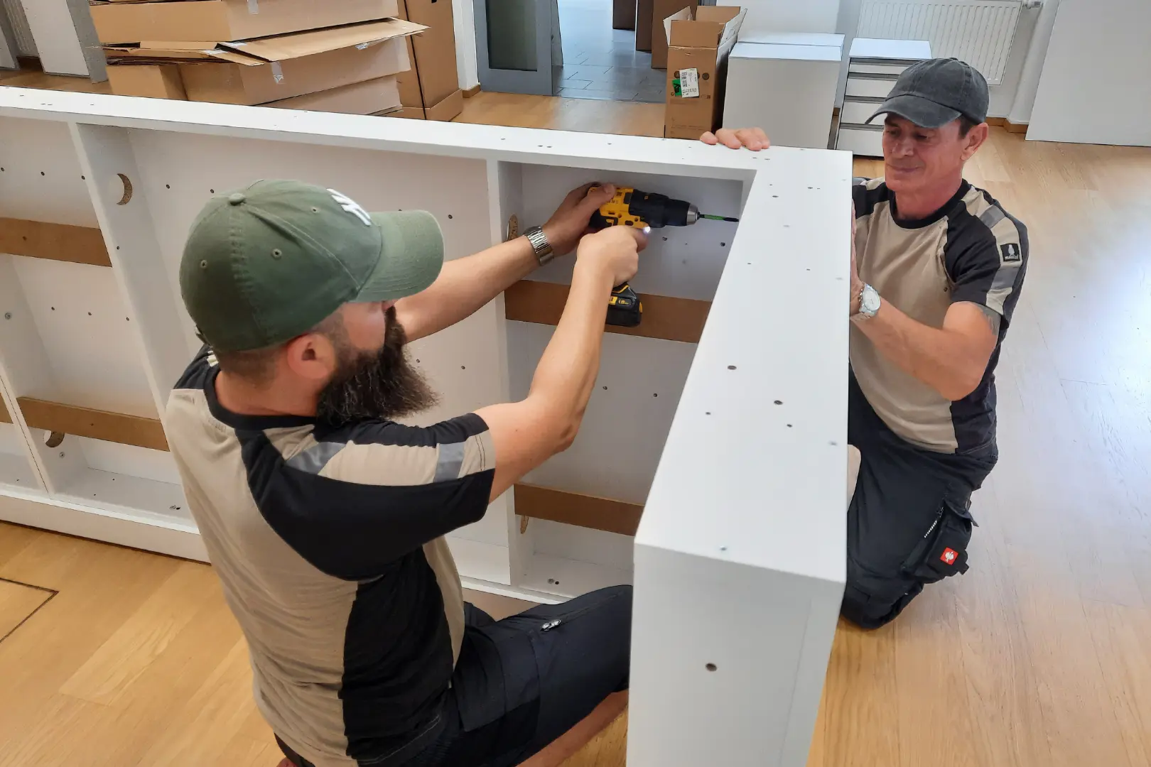 Zwei Mitarbeiter von reoffice bei der Montage eines weißen Büromöbels.