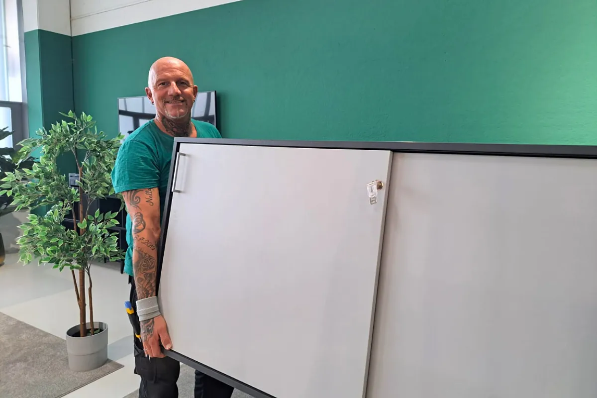 Lächelnder Mitarbeiter trägt einen Büroschrank im Büro