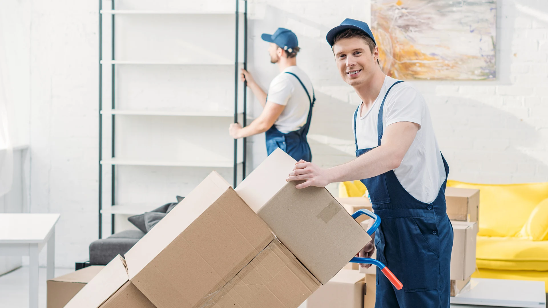 Ein lächelnder Umzugshelfer transportiert Kartons mit einer Handkarre.