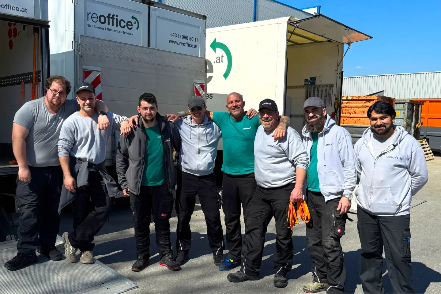 Das Team von reoffice steht lächelnd vor ihren Umzugswagen.